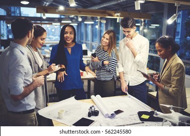 Studying group of male and female designers working in friendly atmosphere creating map of city landscape under orders from skilled leader using wireless connection to internet and modern technologies