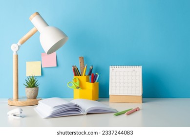 Study-ready arrangement: side view photo of a desk showcasing school essentials, such as stationery holder, book, lamp, calendar and more on blue wall backdrop. Empty space for text or promo messages - Powered by Shutterstock