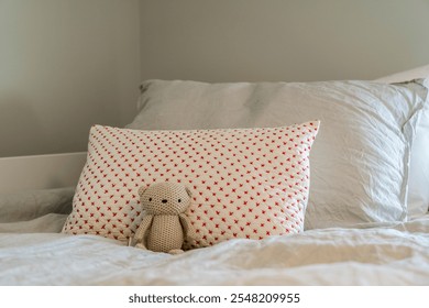 A stuffed animal is sitting on a pillow on a bed. The pillow is white and has a pattern of red and white dots. The stuffed animal is a teddy bear and is placed on the pillow in the middle - Powered by Shutterstock