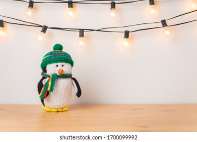 Stuffed animal toy penguin on wood surface with string lights