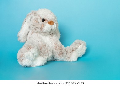 Stuffed bunny on blue background. Easter concept. Cute white toy bunny sitting on colored background.