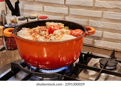 Stuffed cabbage rolls and stuffed tomatoes are cooked in saucepan on gas stove.