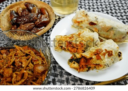 Stuffed chicken flatbread wraps served with sweet dates, spicy curry and herbal tea on traditional dining table. Authentic halal cuisine concept for Ramadan iftar and festive meals.