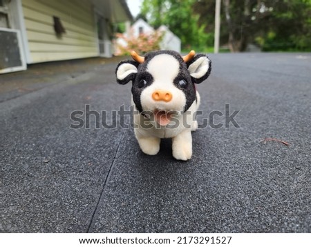 A stuffed cow standing on a shingled rooftop. 