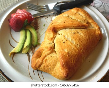 stuffed croissant with avocado and strawberry on a white plate with knife and fork
					