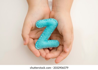 Stuffed Felt Letter Of The Alphabet In Open Hands Of Child. Kid Holding Handmade Capital Letter 