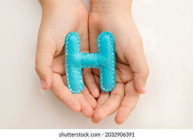 Stuffed Felt Letter Of The Alphabet In Open Hands Of Child. Kid Holding Handmade Capital Letter 