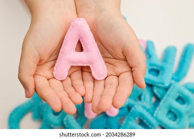 Stuffed Felt Letter Of The Alphabet In Open Hands Of Child. Kid Holding Pink Color Handmade Capital Letter 