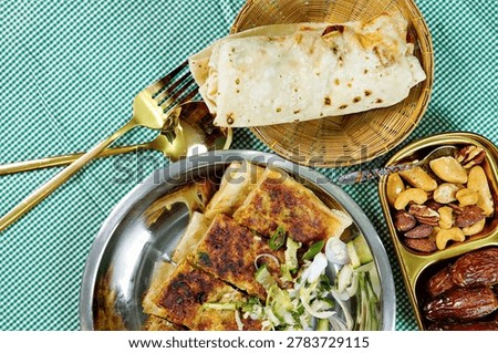 Stuffed flatbread served with crispy snacks, fresh salad and mixed nuts on festive dining table. Authentic halal street food concept for Ramadan meals and Middle Eastern cuisine themes.