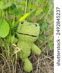 A stuffed frog is peeking around the plants to say hello