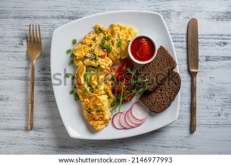 Stuffed omelette with onions, tomato, pepper, eggs and cheese in plate on white wooden background with a knife and fork. Healthy diet food for breakfast. Tasty morning food. Top view, close up