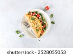 Stuffed omelette with tomatoes, cheese and spinach on a white background. Top view.