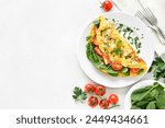 Stuffed omelette with tomatoes and spinach over light stone background with copy space. Top view, flat lay