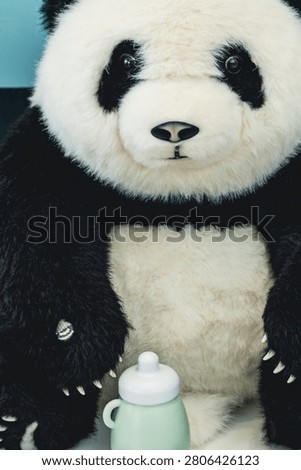 Stuffed panda bear toy with plastic baby bottle on table surface