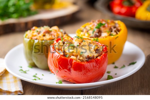 Stuffed peppers, halves of\
peppers stuffed with rice, dried tomatoes, herbs and cheese in a\
baking dish on a blue wooden table, top view. (Turkish name; biber\
dolmasi)
