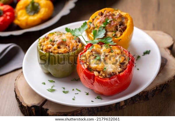 Stuffed peppers, halves of\
peppers stuffed with rice, dried tomatoes, herbs and cheese in a\
baking dish on a blue wooden table, top view. (Turkish name; biber\
dolmasi)