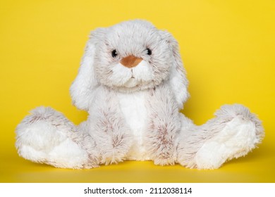 Stuffed soft toy bunny on yellow background. Easter concept. Beautiful white toy bunny sitting on colored background.
