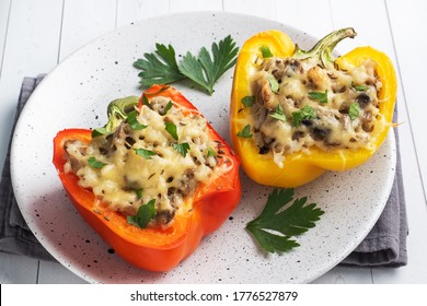 Stuffed sweet peppers with rice mushrooms and cheese with herbs. Baked halves of red and yellow peppers with filling. White wooden background. - Powered by Shutterstock