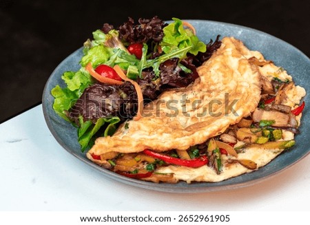 Stuffed Vegetable Omelette with Mixed Leaf Salad. Bright cherry tomatoes and colorful peppers. Perfect for healthy menus, breakfast, cooking blogs.