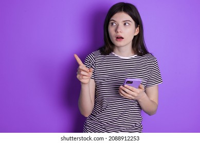 Stunned Caucasian woman wearing striped T-shirt isolated over studio background points sideways right copy space, recommends product, sees astonishing thing