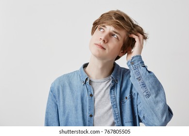 Stunned fair haired man with blue eyes, looks with puzzled expression up, tries to remember something important. Pensive dreamy young man poses indoors