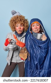 Stunned Female Campers Spend Free Time In Nature During Cold Winter Day Carry Woood To Make Campfire Stare Impressed At Camera Try To Warm Themselves With Hot Drink Isolated Over Blue Background