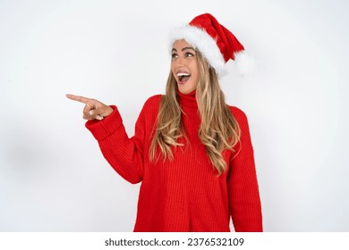 Stunned Young beautiful woman wearing christmas hat over white studio background with greatly surprised expression points away on copy space, indicates something - Powered by Shutterstock