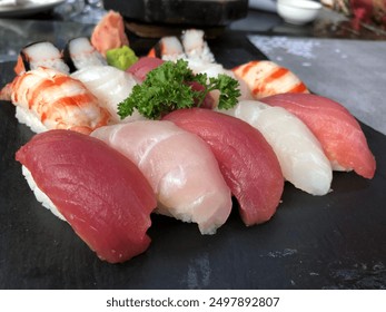 A stunning 14-piece nigiri sushi assortment on a black tray, garnished with parsley. Enjoy a variety of prawns, crab sticks, tuna, red snapper, and salmon, complemented by ginger and wasabi. - Powered by Shutterstock