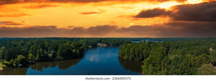 a stunning aerial panoramic shot of the blue waters of Lake Peachtree with vast miles of lush green trees and boats docked along the lake with powerful clouds at sunset in Peachtree City Georgia USA
