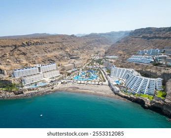 A stunning aerial perspective of Gran Canaria’s cliffside resorts featuring luxurious accommodations, a vibrant waterpark, and a sandy beach along the azure Atlantic Ocean. - Powered by Shutterstock