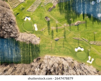 Stunning aerial perspective showcasing a well-maintained golf course with manicured greens, sand traps, and water hazards, nestled among trees during daytime.