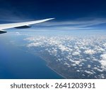 Stunning aerial view from an airplane wing, revealing a vast ocean, cloud formations, and distant land. Ideal for travel, aviation, or nature themes. #AerialPhotography #OceanView #Cloudscape