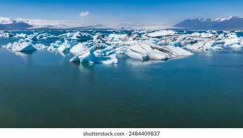 Stunning aerial view of a deep blue glacial lagoon in Iceland, featuring scattered white and blue icebergs and snow-covered mountains in the background. - Powered by Shutterstock