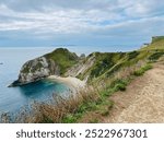 A stunning aerial view of Durdle Door Beach with turquoise waters shimmering below. The beach curves gracefully along the coastline, framed by the iconic cliffs and lush green landscape