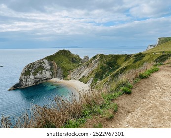 A stunning aerial view of Durdle Door Beach with turquoise waters shimmering below. The beach curves gracefully along the coastline, framed by the iconic cliffs and lush green landscape - Powered by Shutterstock