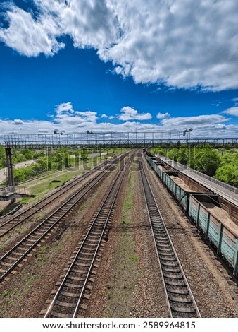 A stunning aerial view of expansive railroad tracks stretching into the distance under a bright blue sky. fluffy clouds add depth to the scene, while lush green trees line the tracks, creating a