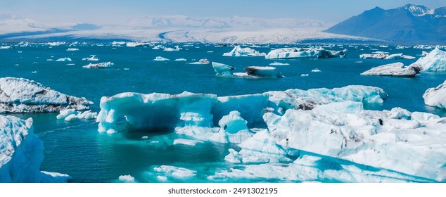Stunning aerial view of a glacial lagoon in Iceland, featuring brilliant blue water, white and blue icebergs, and a barren rocky landscape with distant mountains. - Powered by Shutterstock
