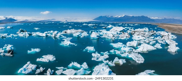 Stunning aerial view of a glacial lagoon in Iceland, featuring floating icebergs, turquoise water, and snow-covered mountains under a clear blue sky. - Powered by Shutterstock
