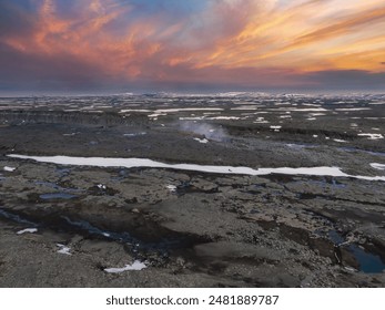 Stunning aerial view of Iceland's rocky, barren landscape with patches of snow. The sky is a beautiful mix of pink and orange, reflecting the colors of the sunset. - Powered by Shutterstock