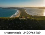 A stunning aerial view of Palm Beach, Sydney, coastal lighthouse at sunset, showcasing the surrounding landscape of beach, ocean, and hills.