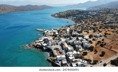 Stunning aerial view of Plaka Beach in Crete,  with the view of Spinalonga showcasing the vibrant turquoise waters, a serene sailboat, rocky cliffs, and whitewashed houses nestled along the coastline - Powered by Shutterstock