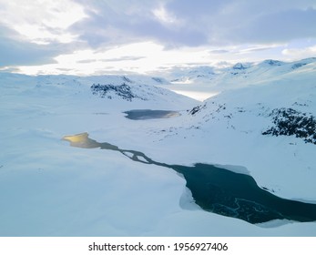 Stunning aerial view of a river flowing through a snow covered tundra and mountain range.