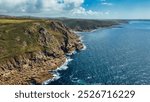 A stunning aerial view of rugged cliffs along a coastline, with clear blue waters and a bright sky. At Cape Cornwall, UK.