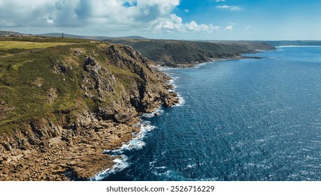 A stunning aerial view of rugged cliffs along a coastline, with clear blue waters and a bright sky. At Cape Cornwall, UK. - Powered by Shutterstock