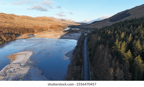 A stunning aerial view of the Scottish Highlands featuring dramatic mountains, a serene blue lake, lush green valleys, and scattered low-lying clouds under a bright sky - Powered by Shutterstock