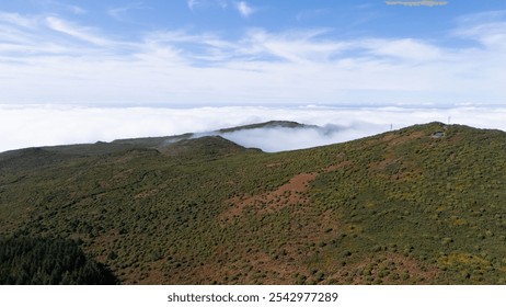 A stunning aerial view of a verdant mountain range partially covered by clouds, under a serene blue sky. Perfect for depicting natural beauty and tranquility. - Powered by Shutterstock