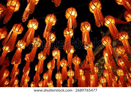 A stunning array of orange Lanna-style paper lanterns illuminating the night sky during the Yi Peng or Loy Krathong festival, creating a magical warm glow and festive backdrop.