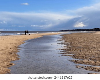 Stunning beautiful coast landscape of white sandy beach at low tide inlet river on shore to horizon with couple walking blue sky calm sea and white cloud Spring cold fresh day at Winterton Norfolk uk  - Powered by Shutterstock