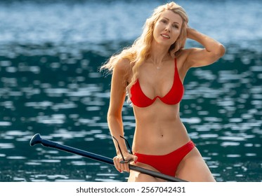 A stunning blonde bikini model glides across a serene lake on a paddleboard, basking in the warmth of the summer sun. The sparkling water and vibrant scenery add to the idyllic, sun-soaked vibe. - Powered by Shutterstock