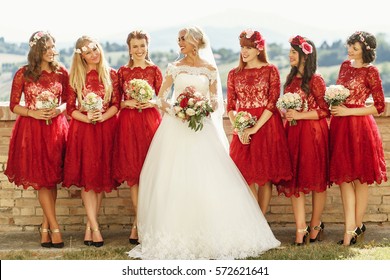 Stunning Blonde Bride And Bridesmaids In Short Red Dresses Pose Before Beautiful Landscape